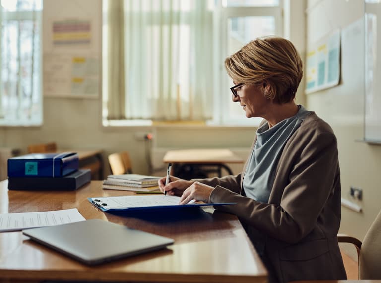 Mature female teacher grading exam papers at high school.