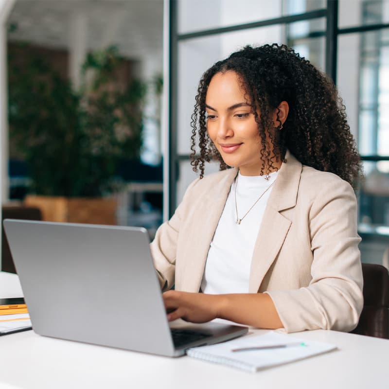 Woman uses laptop. Successful curly haired Hispanic or Brazilian woman in stylish elegant clothes, office employee, secretary or hr manager, using a laptop while sitting at her workplace, working.
