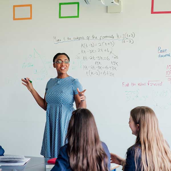 Teacher standing at whiteboard teaching secondary pupils