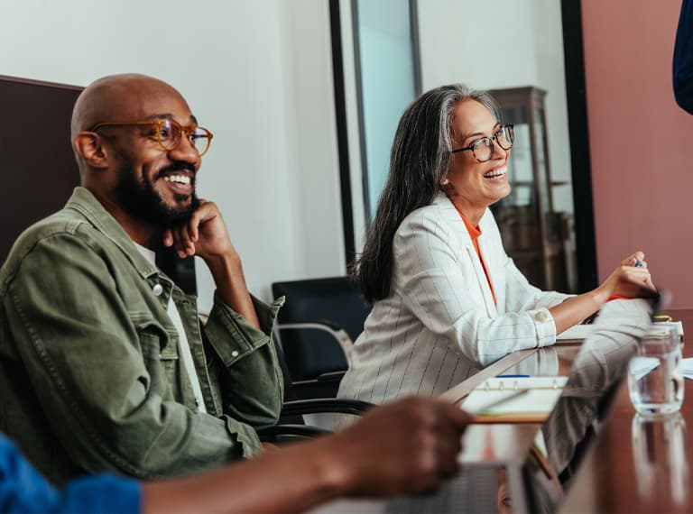 Colleagues in a modern boardroom having a casual office meeting, laughing and happy. The atmosphere is engaging and lighthearted.