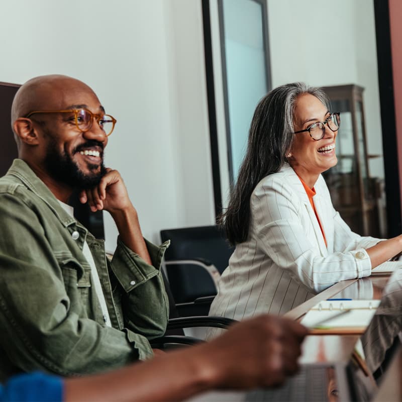 Colleagues in a modern boardroom having a casual office meeting, laughing and happy. The atmosphere is engaging and light-hearted.