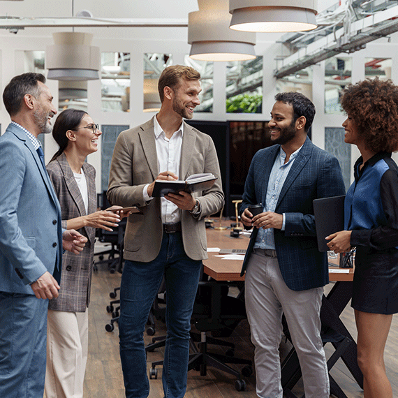 Five diverse professionals in business attire gather in a modern office, with a man holding an open book at the center.