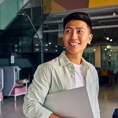Young professional smiling while holding a laptop in a modern office space with colorful walls.