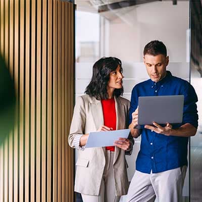 Two professionals reviewing documents and laptop in modern office with wooden slat wall feature.